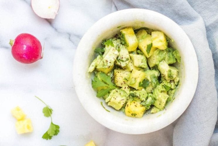 Avocado and radishes displayed in a white bowl.