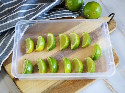 Lime wedges spaces out in a plastic tray on a wooden board background