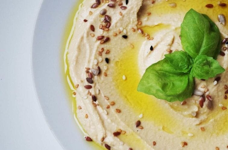 A bowl of frozen hummus with a basil leaf on top.