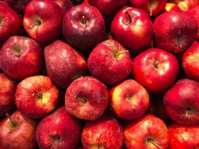 Bright red apples piled next to one another taking up the whole frame of the photo