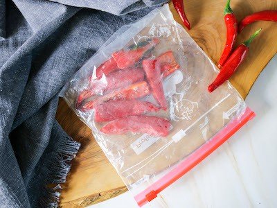 Red chillies sliced lengthways in a sealed freezer bag on a wooden chopping board