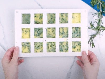 Frozen cubes in an ice cube tray containing frozen coriander and butter