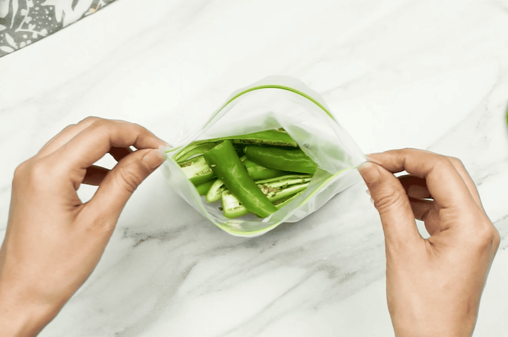 Sliced green chilli halves in an open freezer bag being held open by a woman's hands