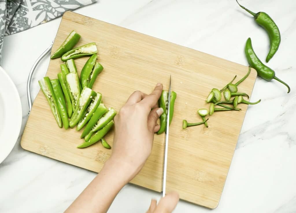 A woman's hands slicing green chillies lengthways to remove the seeds