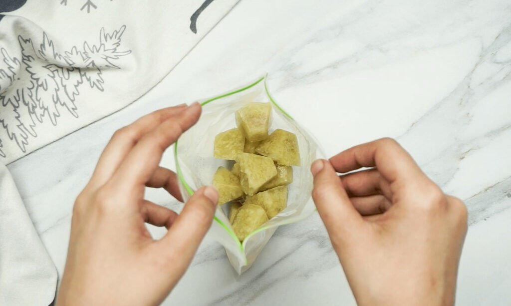 Frozen cubes of ginger inside an open freezer bag being held by a woman's hands