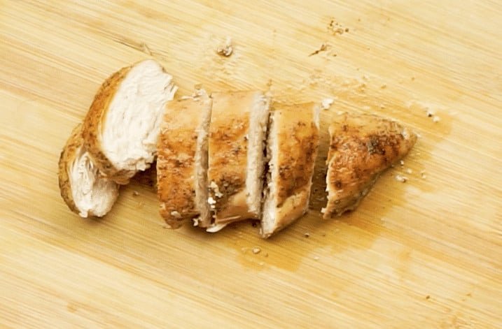 A cooked chicken breast, sliced into 6 evenly-sized pieces on a wooden chopping board