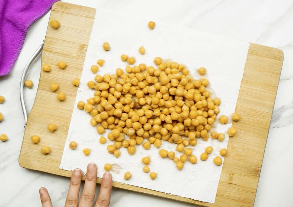 Chickpeas spread out on a white kitchen paper towel on top of a wooden chopping board