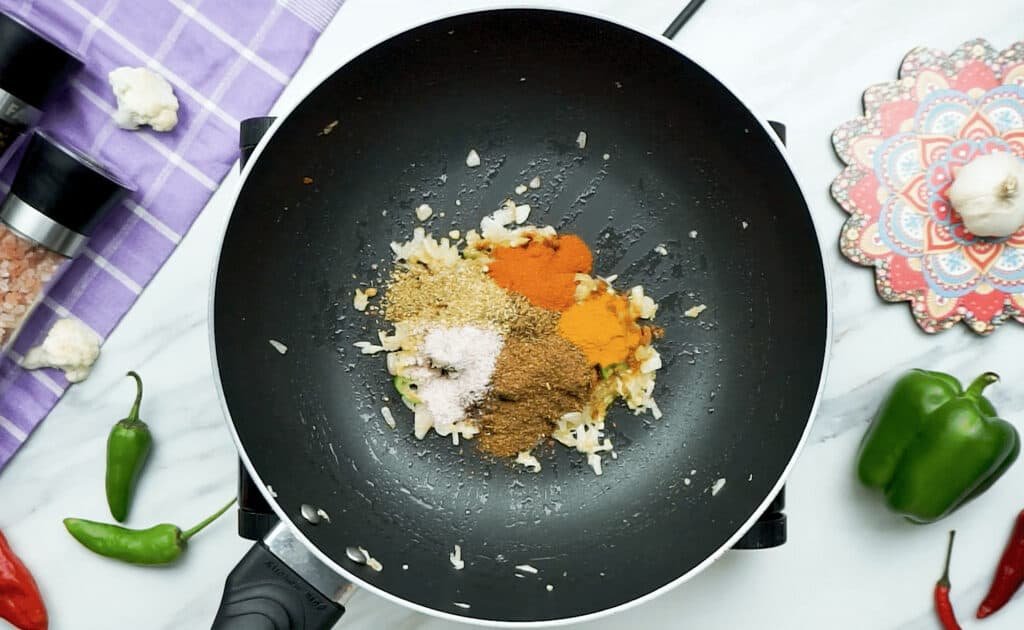 Lot of bright spices on top of onions, ginger and garlic in a skillet for the base of the vegetable curry