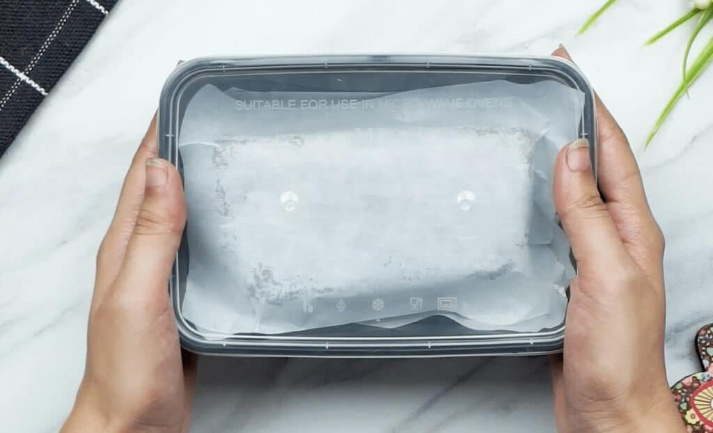 A plastic container, filled with portions of brownis, tightly sealed with a clear plastic lid, being held by a woman's hands ready for the freezer