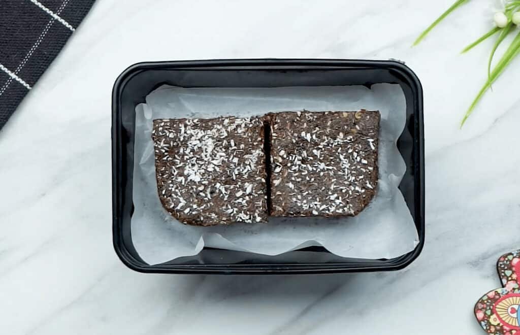 2 brownies placed inside a plastic container, lined with baking paper, ready for the freezer