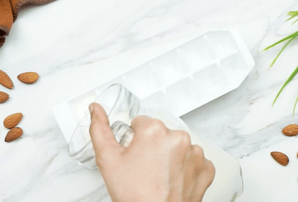 Almond milk being poured into a white ice cube tray on a marble background