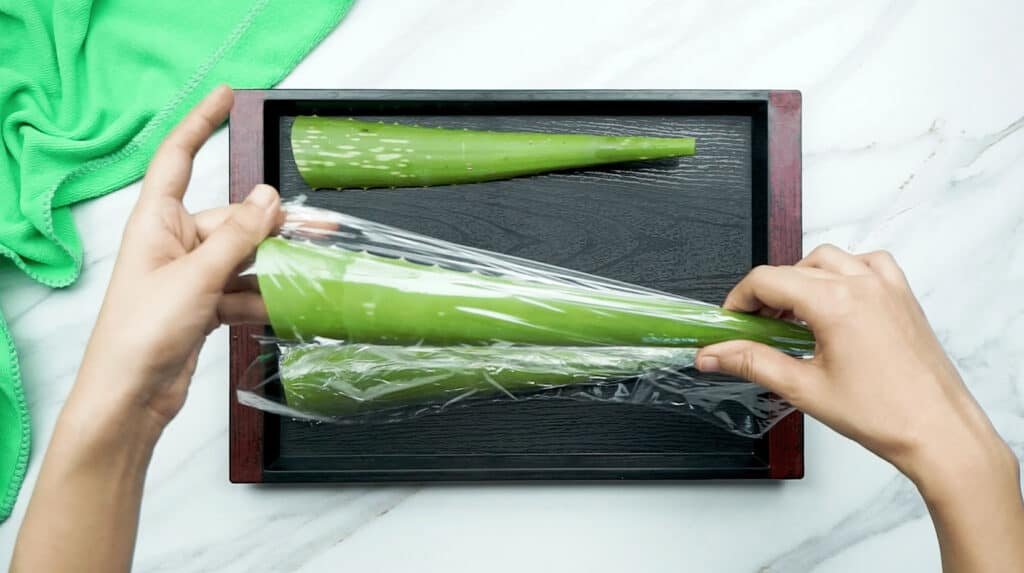 3 leaves from an aloe vera plant being wrapped in cling film in preparation for the freezer