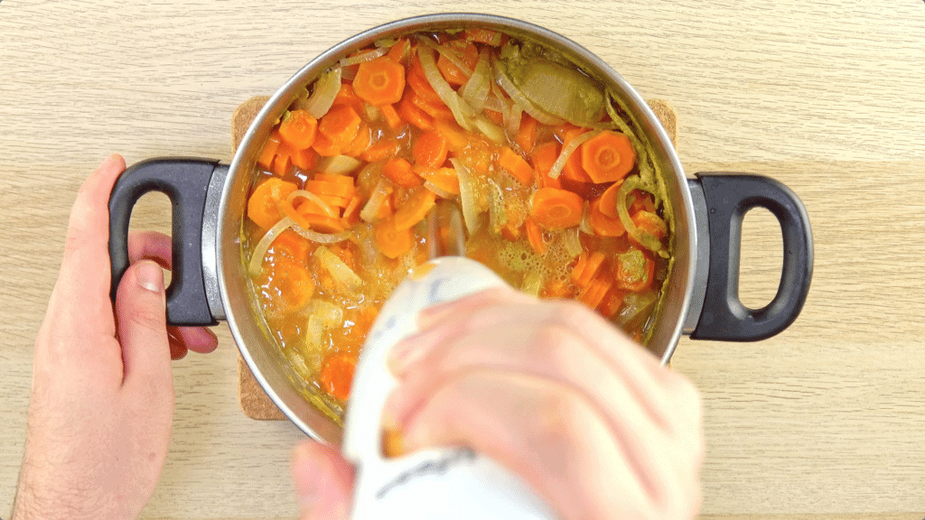 A stick blender blitzing carrot, onions and stock up to make a soup