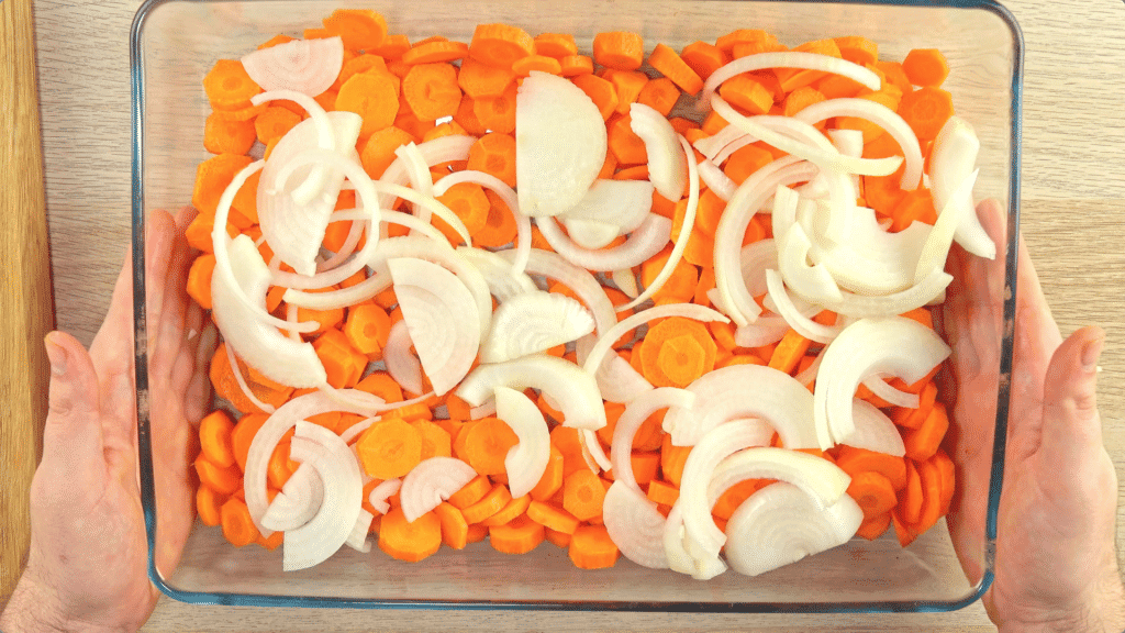 Slices carrots and onions in a glass baking dish 