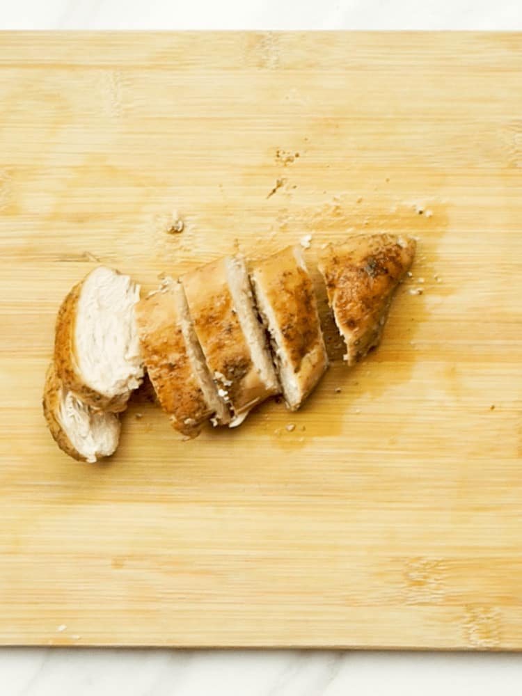 A cooked chicken breast, sliced into 6 pieces, on a wooden chopping board 