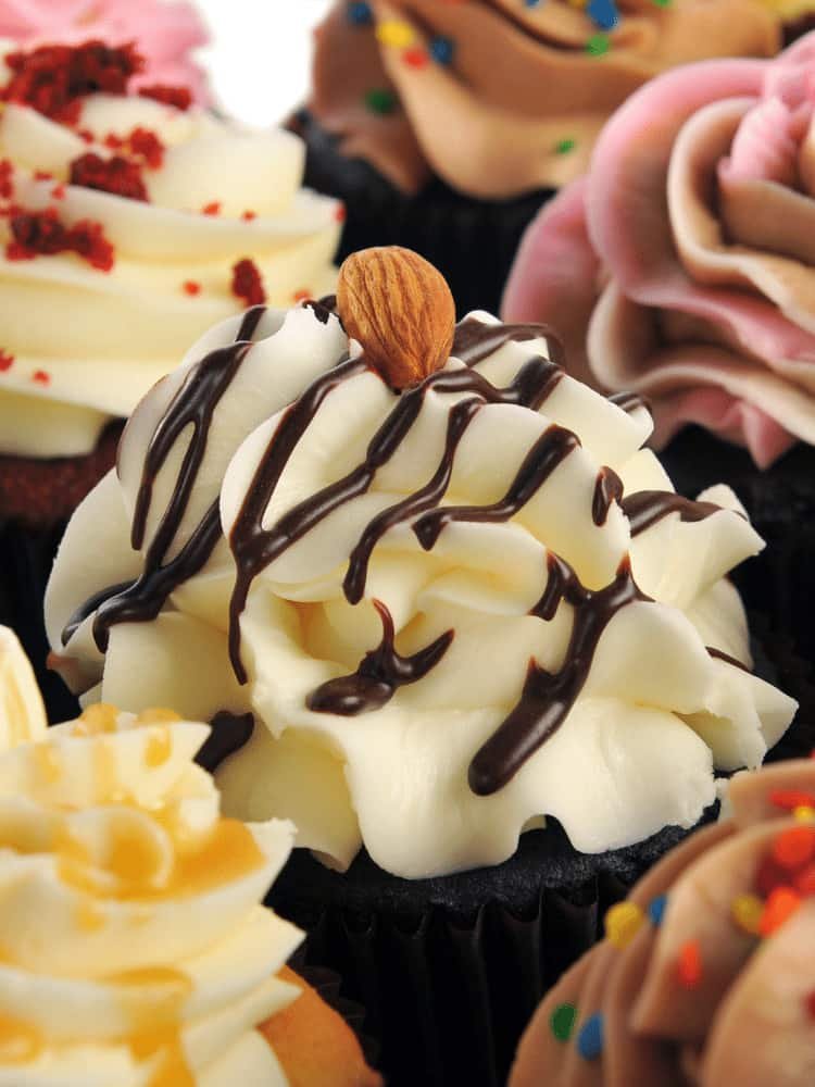 Close up of a cupcake with cream cheese frosting, chocolate sauce and a nut