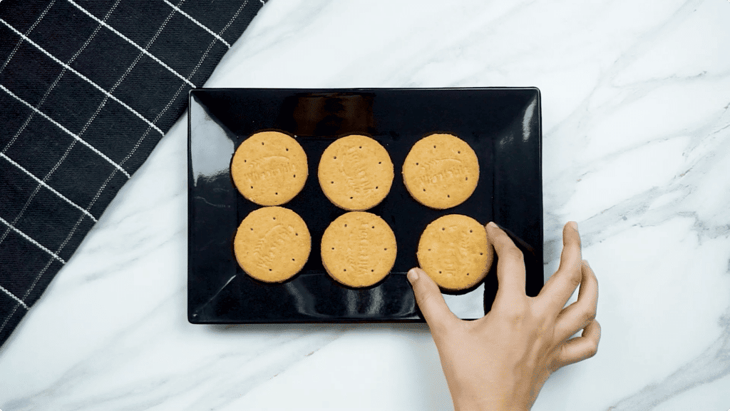 6 digestive biscuits on a black tray with a woman's hand placing 1 of the biscuits onto the tray