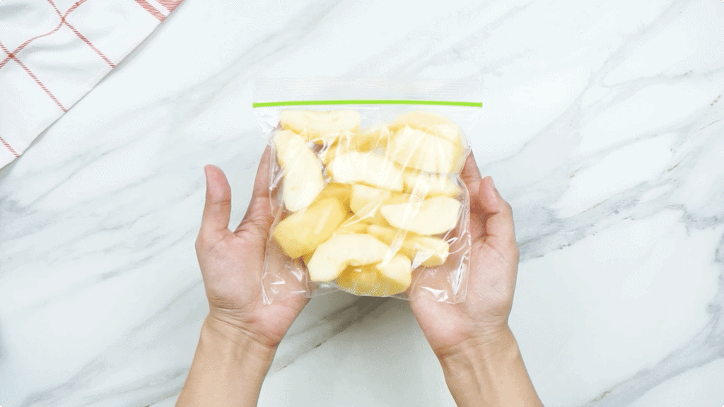 A woman's hands holding a clear freezer bag containing apple slices 