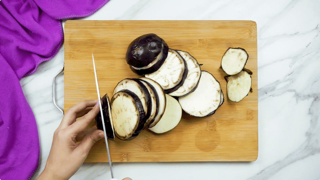 Aubergine being sliced on a wooden chopping board