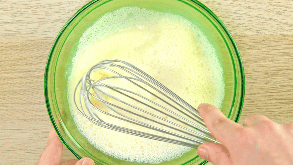 Eggs and milk being whisked in a green-tinted glass bowl