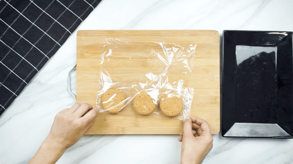 Wrapping 3 digestive biscuits in cling film on a wooden chopping board